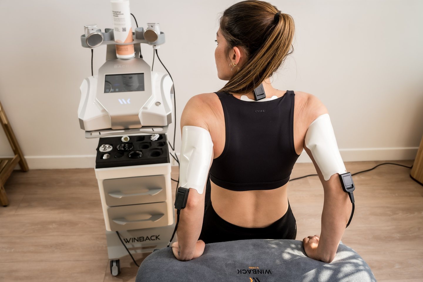Pacientă așezată, cu electrozii Tecar înfășurați pe ambele brațe, lângă consola Winback